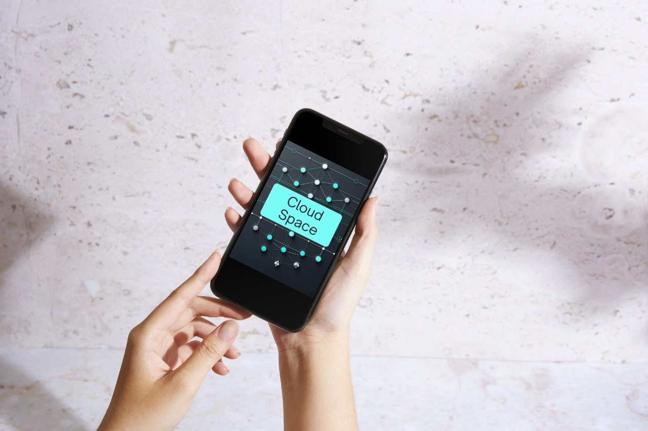 A person holds a black smartphone showing a digital vault key interface on the screen, set against a light textured wall with soft shadows.