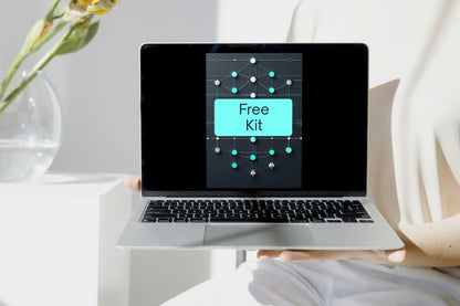 A silver laptop held by a person in a bright, modern room. The laptop screen displays a digital graphic with a cyan label reading 'Free Kit' over a dark network-style design.