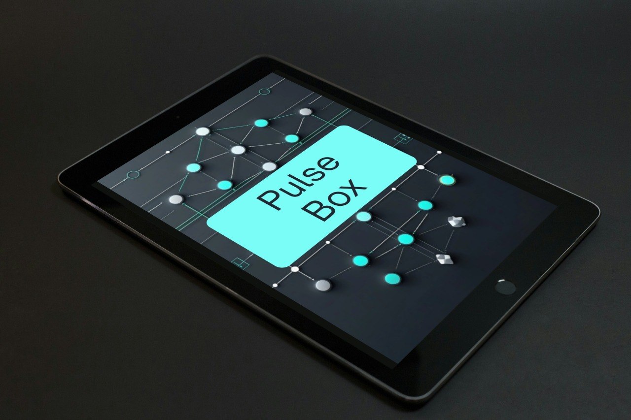 A black tablet device shown at an angle on a dark surface, displaying a digital interface with the words 'Pulse Box' in white text inside a bright cyan box.